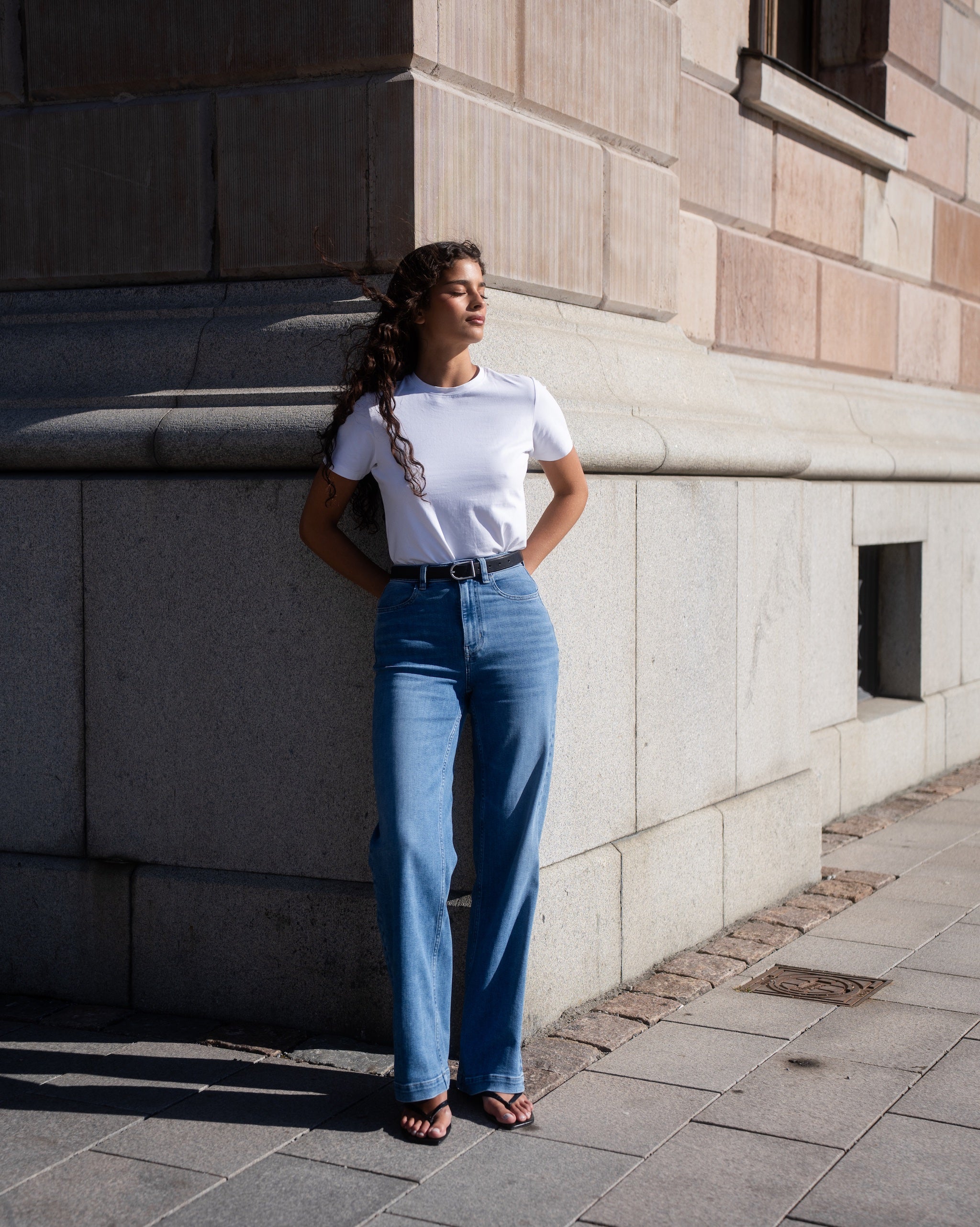 A woman wearing light blue Summer ComfortDenim jeans with a white fitted T-shirt by Ninepine in a clean city-inspired outfit.